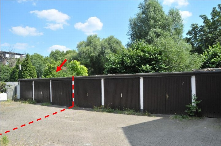Reihenweise angeordnete Garagen mit braunen Holztüren und weißen Pfeilern, gepflasterte Fläche davor, Bäume im Hintergrund
