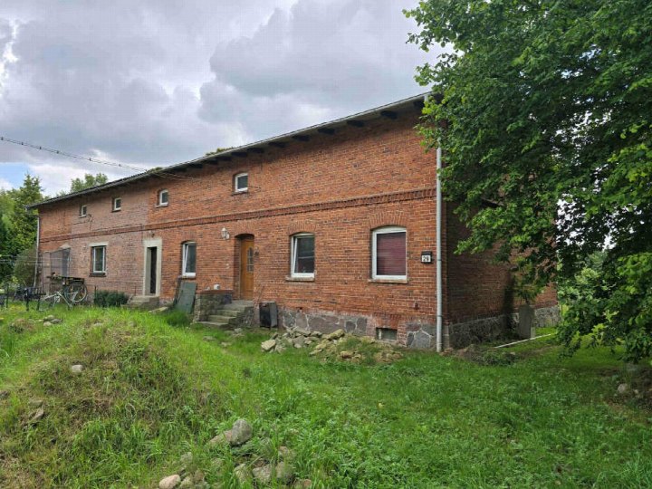 Seitenansicht eines roten Backsteinhauses mit mehreren Fenstern, Eingangstür und Grundstück mit Gras und Bäumen, Hermannshöhe 29, Gültz