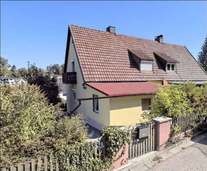 Einfamilienhaus mit Satteldach und gelber Fassade, Vorderansicht mit Balkon und Eingangstor, umgeben von Grünanlagen, Waldstraße 3, Ergoldsbach