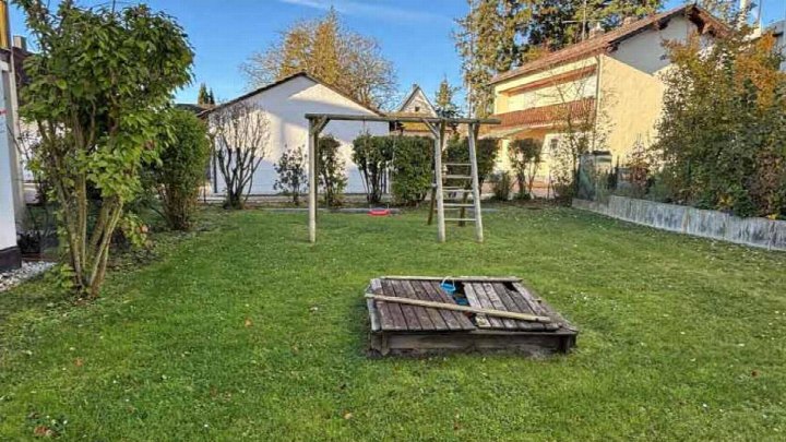Grüner Garten mit Rasen, Sträuchern, Bäumen, Holzspielgerüst und Holzabdeckung über einem Bodeneingang