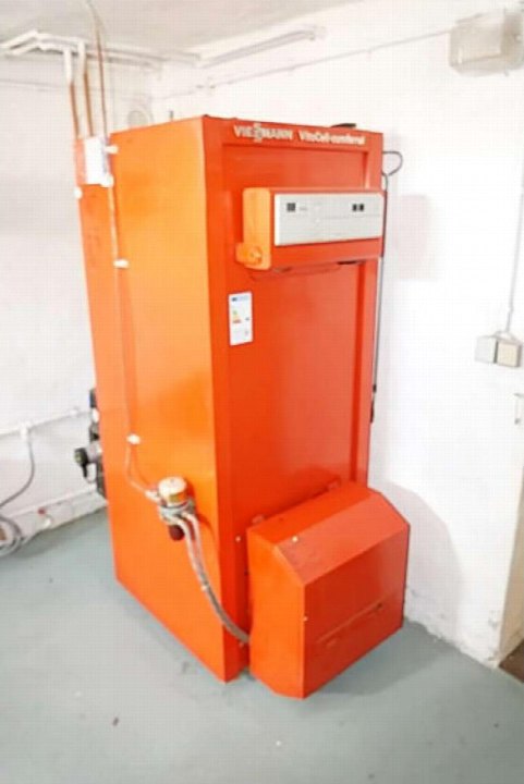 Große orangefarbene Heizungsanlage (VIESSMANN) in einem Keller mit Betonboden und weißen Wänden