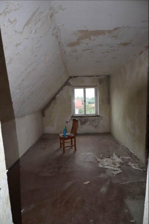 Dachbodenraum mit schrägen Wänden, abblätternder Farbe und einem Fenster; ein Stuhl steht in der Mitte des Raumes