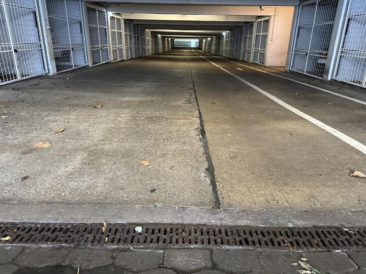 Lange, überdachte Garage mit mehreren verschlossenen Stellplätzen an beiden Seiten, Betonboden und Abflussgitter im Vordergrund