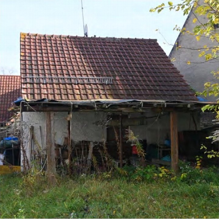 Seitenansicht eines Einfamilienhauses mit Ziegeldach und überdachtem Bereich, umgeben von Grünflächen und Pflanzen