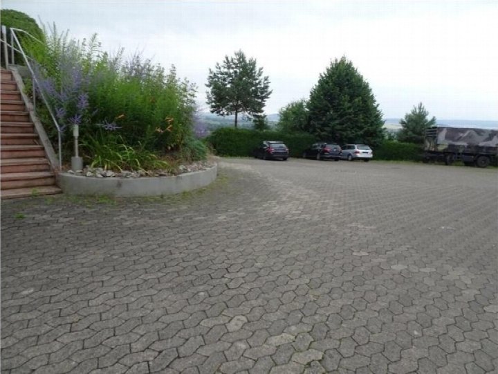Pflasterplatz mit geparkten Fahrzeugen und Anliegerparkplatz neben einer Treppe und Grünanlage