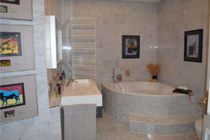 Badezimmer mit Eckbadewanne, Waschtisch, Spiegel und Wandbildern an Marmorwänden