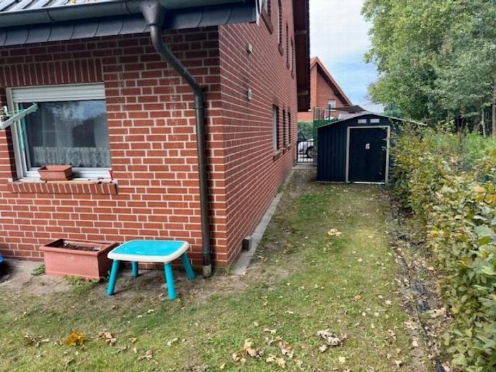 Gartenbereich eines Einfamilienhauses mit Rasen, kleinen Pflanzkübeln, einem Kindertisch und einem Gartenhäuschen im Hintergrund