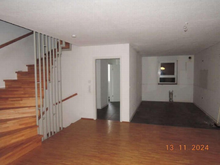 Leerer Wohnbereich mit Holzboden, Treppenhaus mit Metallgeländer und offener Tür zu einem weiteren Raum