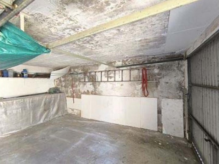 Garage mit Betonboden, Metallrolltor und aufbewahrten Gegenständen wie Leiter und Plane