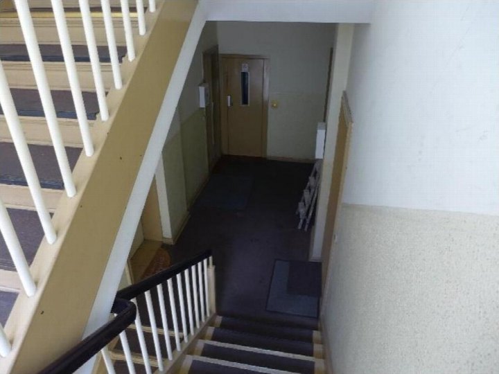 Treppenhaus mit weißer Geländerverkleidung und dunklem Teppichboden, Blick auf einen Flur mit Tür am Ende