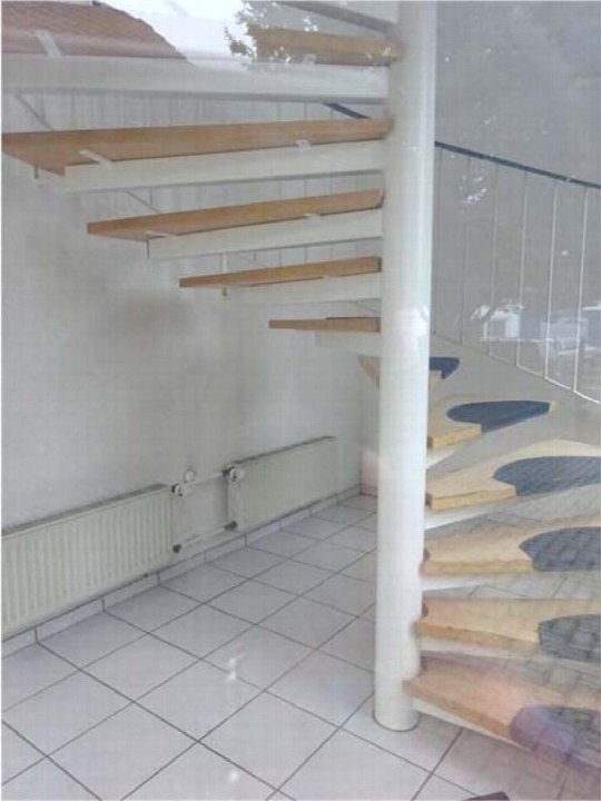 Innenraum mit Wendeltreppe, Holzstufen, weißer Mittelsäule, Fliesenboden und Heizkörper an der Wand
