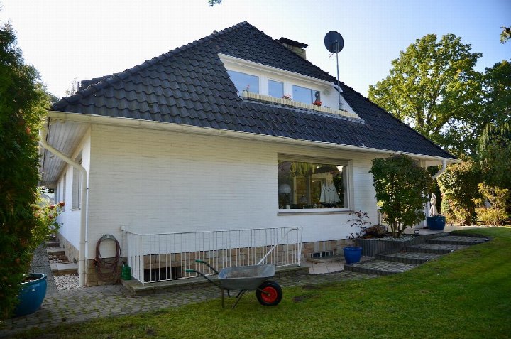 Seitenansicht eines Einfamilienhauses mit dunklem Ziegeldach, weißer Fassade, Fenster, Garten und Gartengeräten in Stuhr, Blockener Straße 6