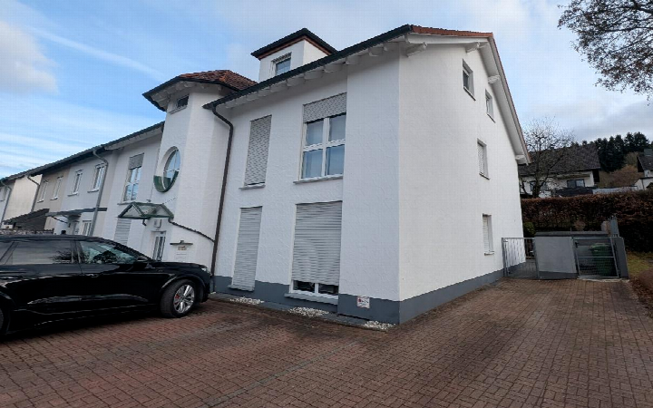 Seitenansicht eines weißen Mehrfamilienhauses mit Fenstern, Rollläden und Ziegeldach in Sundern, Wilhelm-Hauff-Str. 35