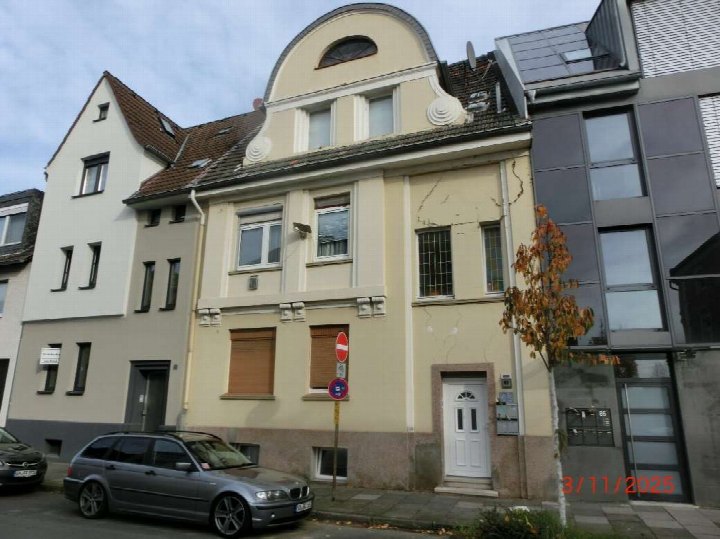 Vorderansicht eines Mehrfamilienhauses in Siegburg, Hohenzollernstraße 83, mit Eingang, Fenstern und Dachgauben. Links geparkter Kombi