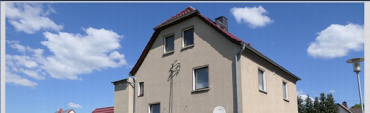 Fassade eines Zweifamilienhauses mit rotem Satteldach, mehreren Fenstern und Schornstein unter blauem Himmel