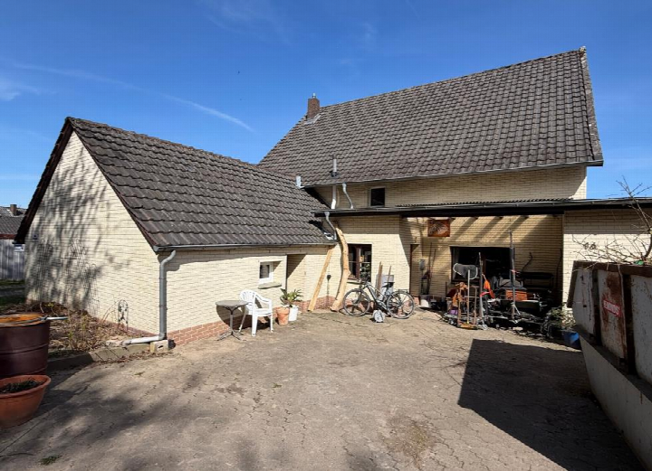 Hinterhof eines Einfamilienhauses mit Garage, Fahrrad und Werkzeugen, gepflastertem Hof und Nebengebäude unter klarem Himmel