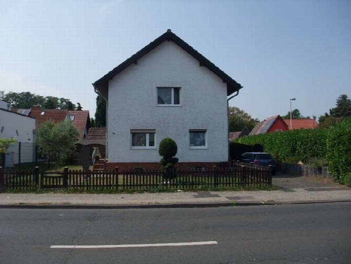 Einfamilienhaus mit weißer Fassade, dunklem Satteldach und Vorgartenzaun, Ansicht von der Straße aus