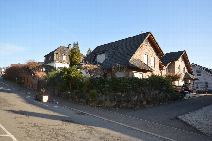 Seitenansicht eines Einfamilienhauses in Neuenrade, Landwehr 2e, mit Gartenmauer, Hecke und angrenzenden Häusern unter klarem Himmel