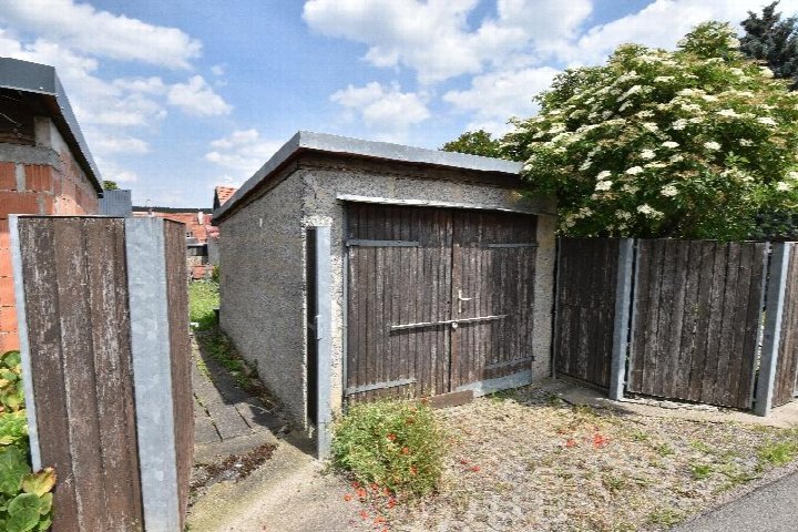 Garage aus Beton mit Holztür im Gartenbereich eines Einfamilienhauses in Ilmenau, umgeben von Holzzaun und Grünanlagen