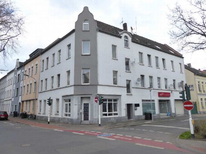 Eckhaus in Krefeld, Peter-Lauten-Straße 35 / Gutenbergstraße 124, weiß-graue Fassade, Erdgeschoss mit Ladenfronten, Obergeschosse mit Fenstern, Straßenansicht mit Verkehrszeichen
