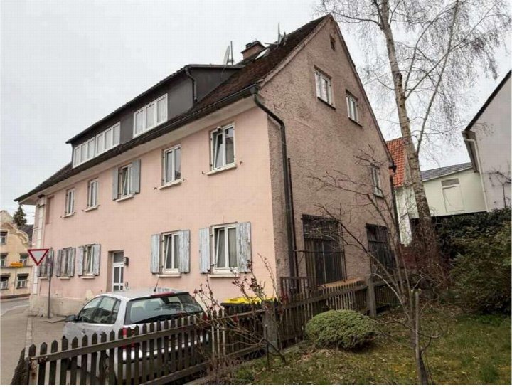 Seitenansicht eines mehrstöckigen Wohnhauses mit rosa Fassade, Dachgauben und Gartenzaun in Ichenhausen, Krumbacher Str. 1