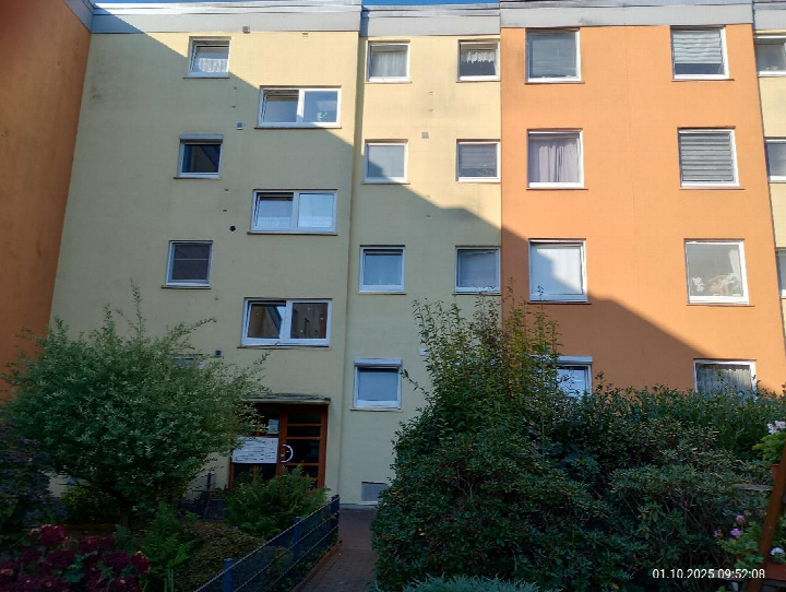 Eingangsbereich eines Mehrfamilienhauses mit gelb-oranger Fassade, Fenstern und Grünanlagen im Vordergrund