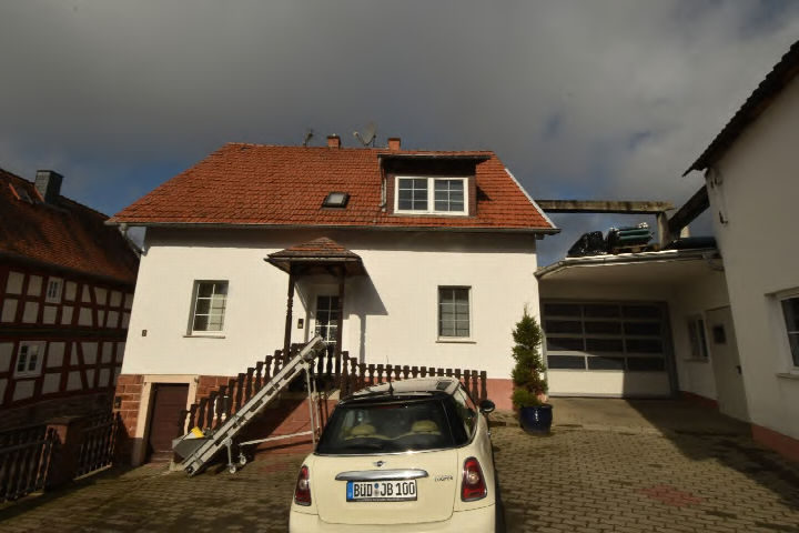 Einfamilienhaus in Büdingen, Burgstraße 8, mit rotem Ziegeldach, weißer Fassade, Eingangstreppe und Garagenanbau. Vor dem Haus steht ein weißer PKW