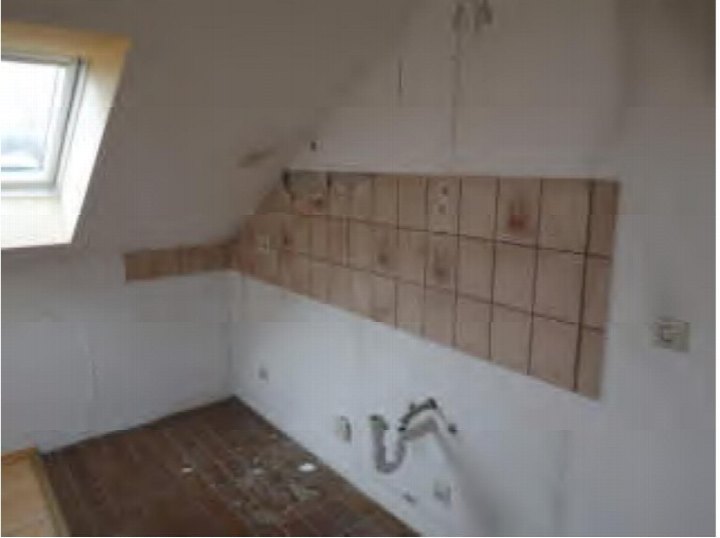 Unfertiger Badezimmerbereich mit Fliesenwand, sichtbaren Rohrleitungen und Dachschräge mit Dachfenster