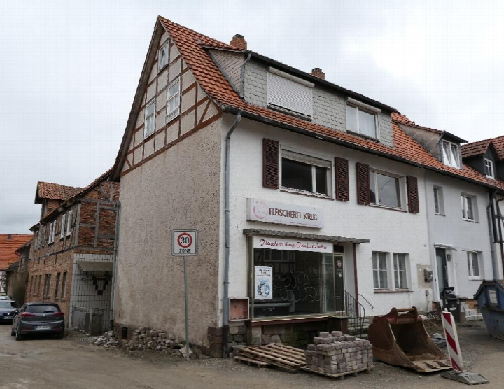 Einfamilienhaus mit Fachwerkdetails und Ladenlokal Fleischerei Krug, Wilhelmsthaler Straße 23, Calden, mit rotem Ziegeldach und Baustellenmaterial vorne