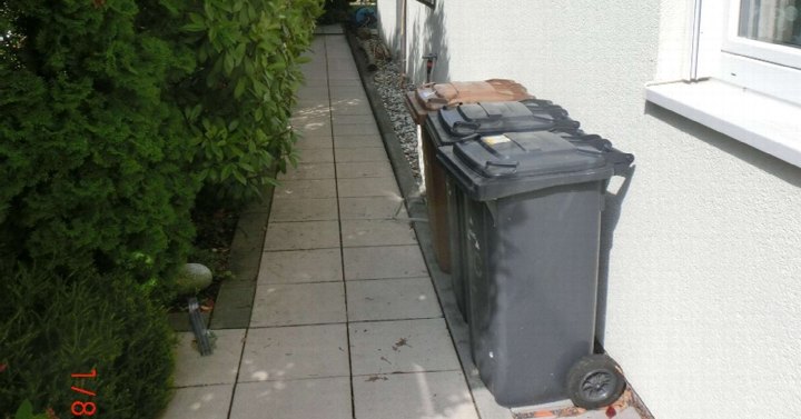 Seitenansicht eines Einfamilienhauses mit gepflastertem Weg, Mülltonnen und Hecke in Hennef, Annostraße 9c