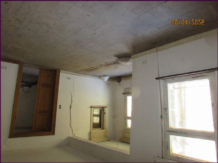 Innenraum eines Einfamilienhauses mit sichtbaren Rissen in Wand und Decke, alten Holztüren und Fenstern, sowie einem veralteten Schrank