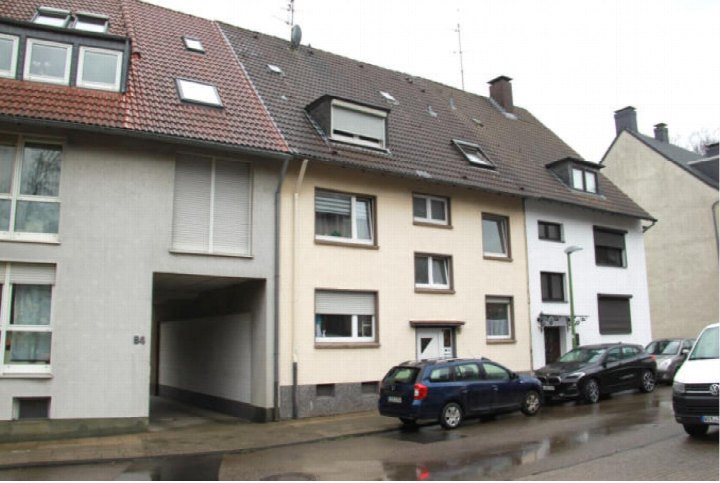 Fassade eines Mehrfamilienhauses mit Satteldach, Fenstern und Einfahrt; geparkte Autos vor dem Gebäude in Essen, Zollstraße 92