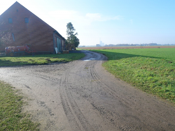 Gravelweg führt an einem roten Backsteinbau vorbei, umgeben von Grünflächen und landwirtschaftlichen Geräten in Petershagen