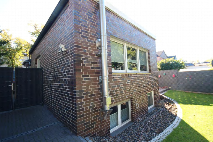 Rückansicht eines Backsteinhauses mit Fenstern, Regenrohr, gepflastertem Bereich und angrenzendem Rasen in Marl, Sickingmühler Straße 81c