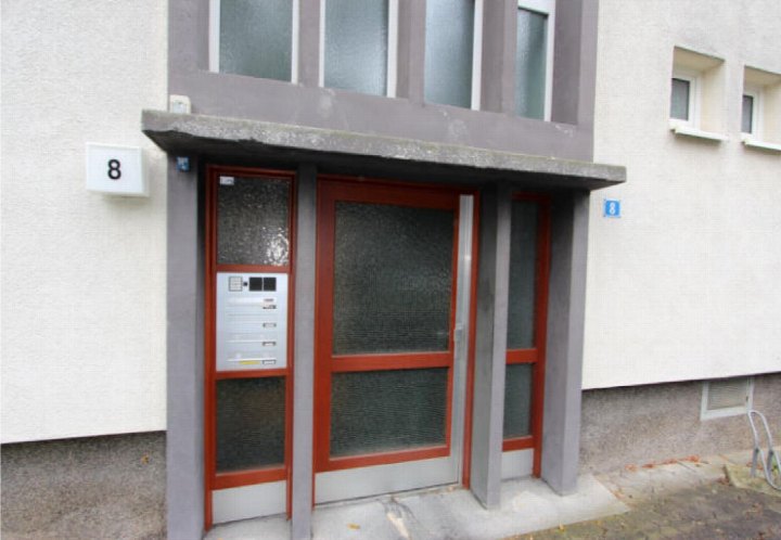 Eingangsbereich der Eigentumswohnung Im Brücherfeld 8 in Köln mit roter Tür, Briefkasten und Hausnummer 8
