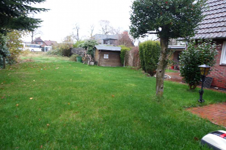 Grüner Garten mit Rasenfläche, Baum, Hecken und kleinem Holzschuppen hinter einem Einfamilienhaus in Westerstede
