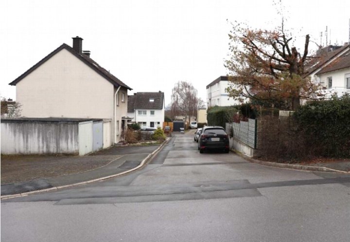 Rückansicht eines Wohnhauses mit Garagen und gepflastertem Weg, umgeben von Bäumen und Nachbarhäusern in Fröndenberg