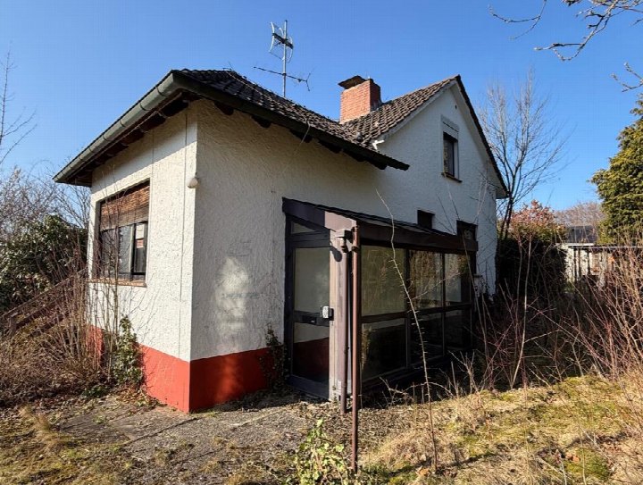 Einfamilienhaus mit weißer Fassade und rotem Sockel, Eingang mit Glasverglasung, Dach mit Schornstein und Antenne, Garten im Vordergrund