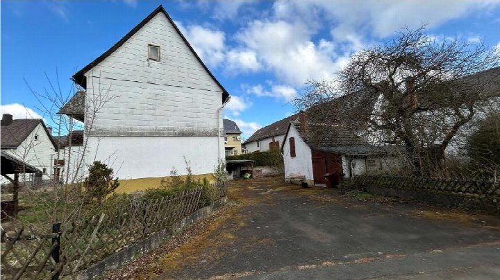 Rückansicht eines weißen Holzgebäudes mit Satteldach, umgeben von weiteren Gebäuden, einem gepflasterten Hof und einem Gitterzaun in Hohenahr, Ringstraße 24