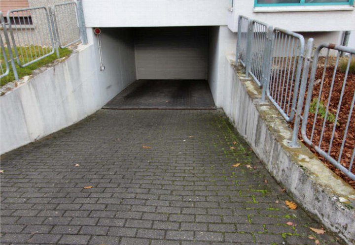 Zugangsrampen zum Untergrundgarage mit Pflastersteinen, Metallgeländern und Betonwänden