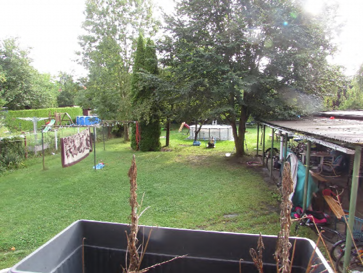 Garten mit Rasenfläche, Bäumen, Spielplatz, Trampolin und überdachter Terrasse im Hinterhof eines Mehrfamilienhauses in Kerpen