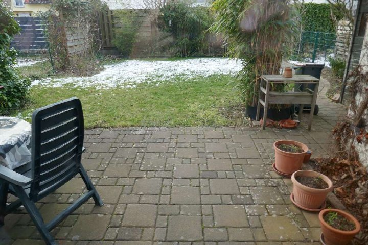 Gartenbereich mit gepflastertem Terrassenbereich, Pflanzenkübeln, Gartenstuhl und Rasenfläche mit leichtem Schneedeck. Köln, Uhuweg 32