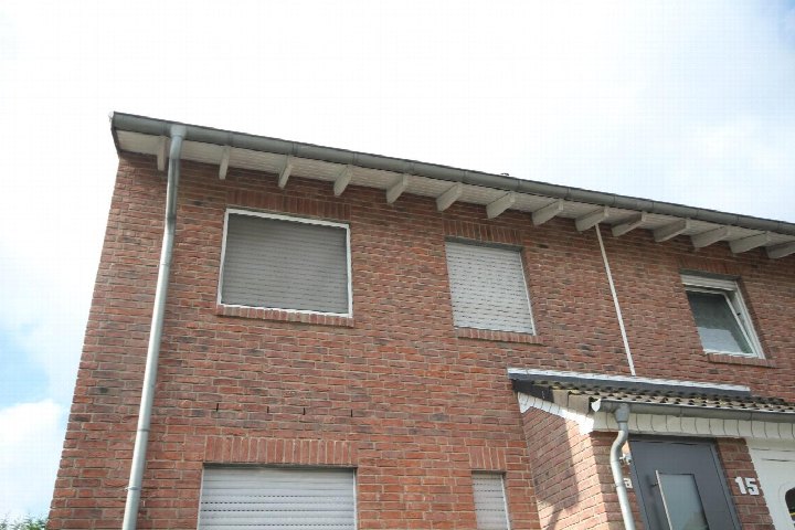 Fassade eines roten Backsteinreihenhauses mit Fenstern, Dachrinne und Hausnummer 15