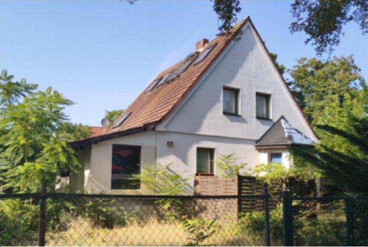 Einfamilienhaus mit Satteldach und Fenstern, umgeben von Bäumen und einem Zaun, Ansicht von vorne