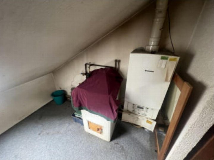 Dachbodenraum mit Heizkessel, abgedeckter Anlage und Eimer, schräge Wände und Decke