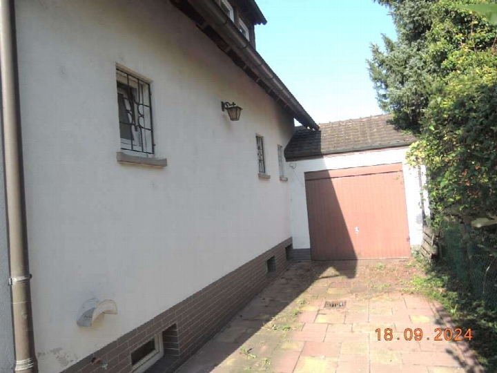 Seitenansicht eines Gebäudes mit weißer Fassade, Fenstern mit Gitter, Wandlampe und angrenzender Garage mit brauner Tür in Limburgerhof, Feuerbachstraße 23