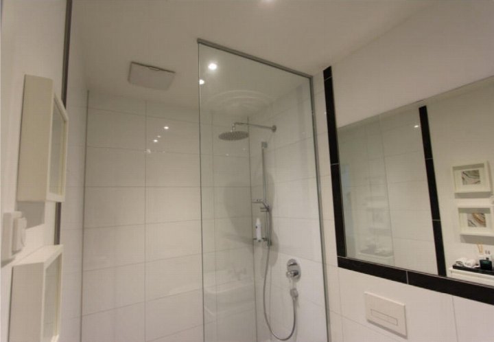 Badezimmer mit Dusche hinter Glasabtrennung, weißen Fliesen und integrierten Ablagen