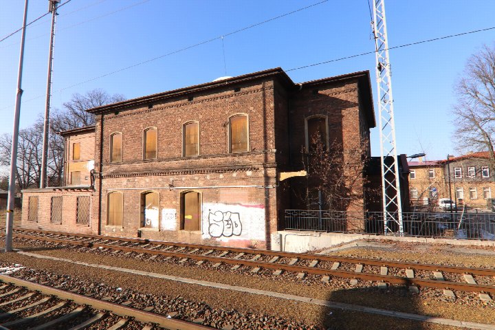 Seitenansicht eines zweistöckigen Backsteinbaus am Bahnhof Ruhland mit Gleisen im Vordergrund und Graffiti an der Fassade