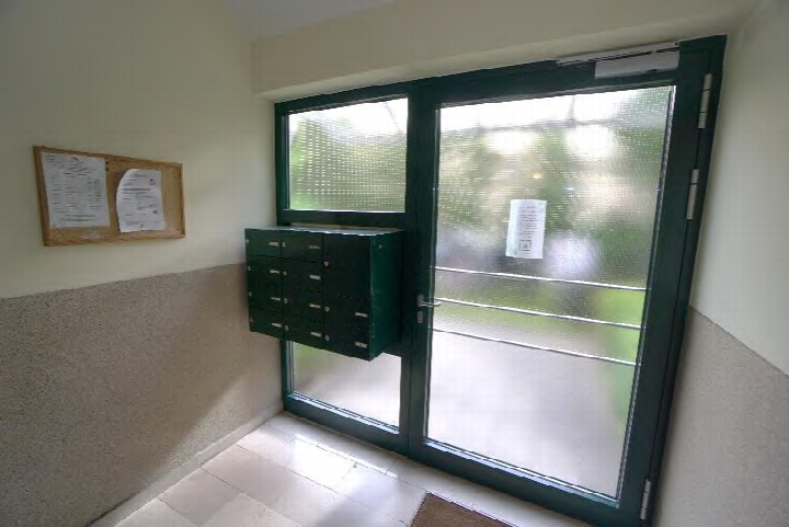 Eingangsbereich mit grüner Glastür, Briefkästen und Anschlagtafel an der Wand