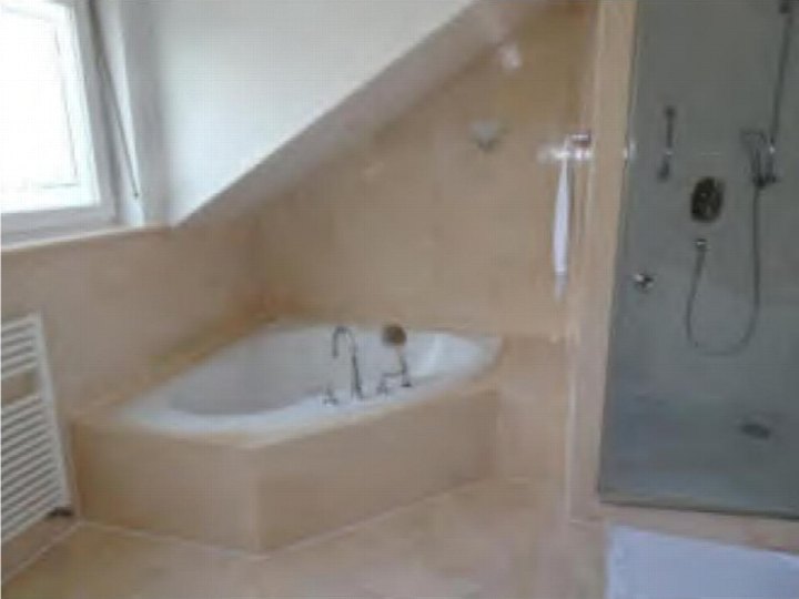 Badezimmer mit Badewanne und Dusche unter schräger Decke, beige Fliesenverkleidung, Fenster links